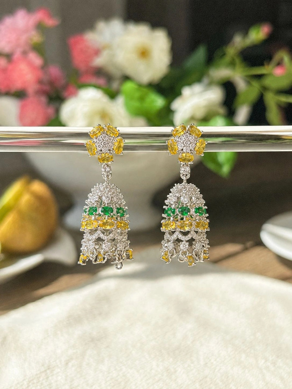Pair of silver CZ chandelier earrings hanging from metal bar with floral backdrop in soft light