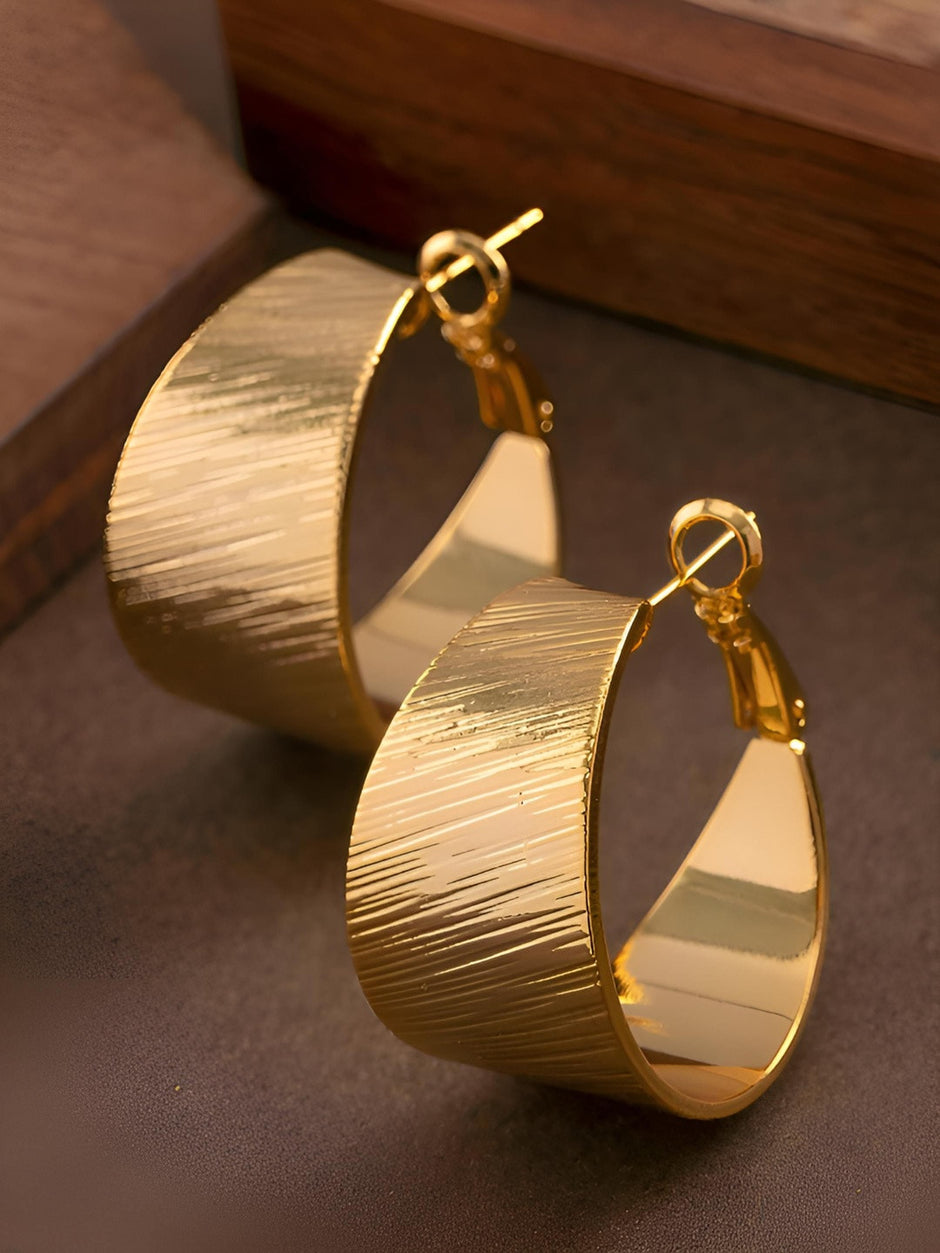 Pair of gold-plated wide band hoop earrings with diagonal line texture on dark brown surface