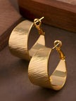 Pair of gold-plated wide band hoop earrings with diagonal line texture on dark brown surface