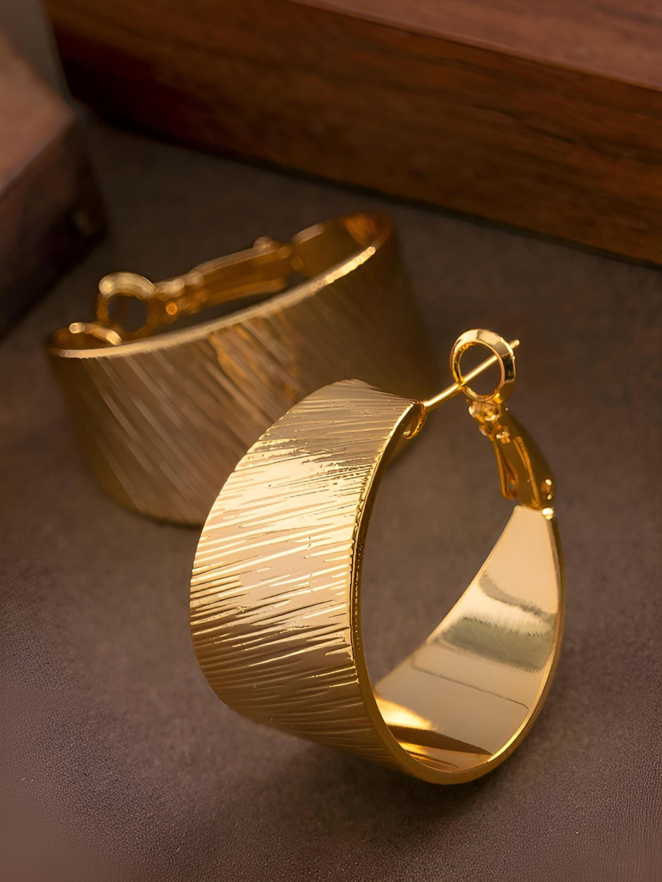Close-up of two gold-plated wide hoop earrings showing latch-back closure and textured outer surface