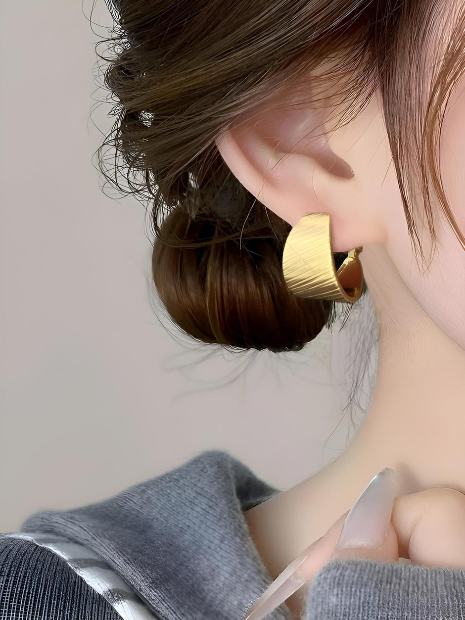 Gold-plated wide hoop earring worn on a woman's ear with dark hair pinned up in a bun