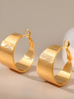 Pair of gold-plated textured wide hoop earrings standing upright on a light grey surface