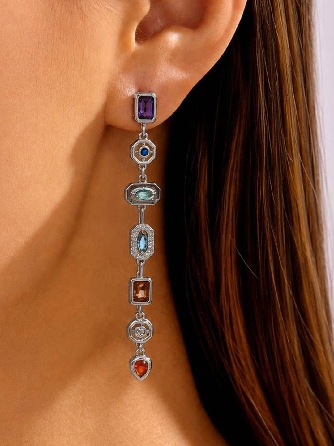 Silver-tone multi-stone long drop earring worn on a woman's ear, showing six geometric stations in purple, blue, teal, aqua, champagne and red