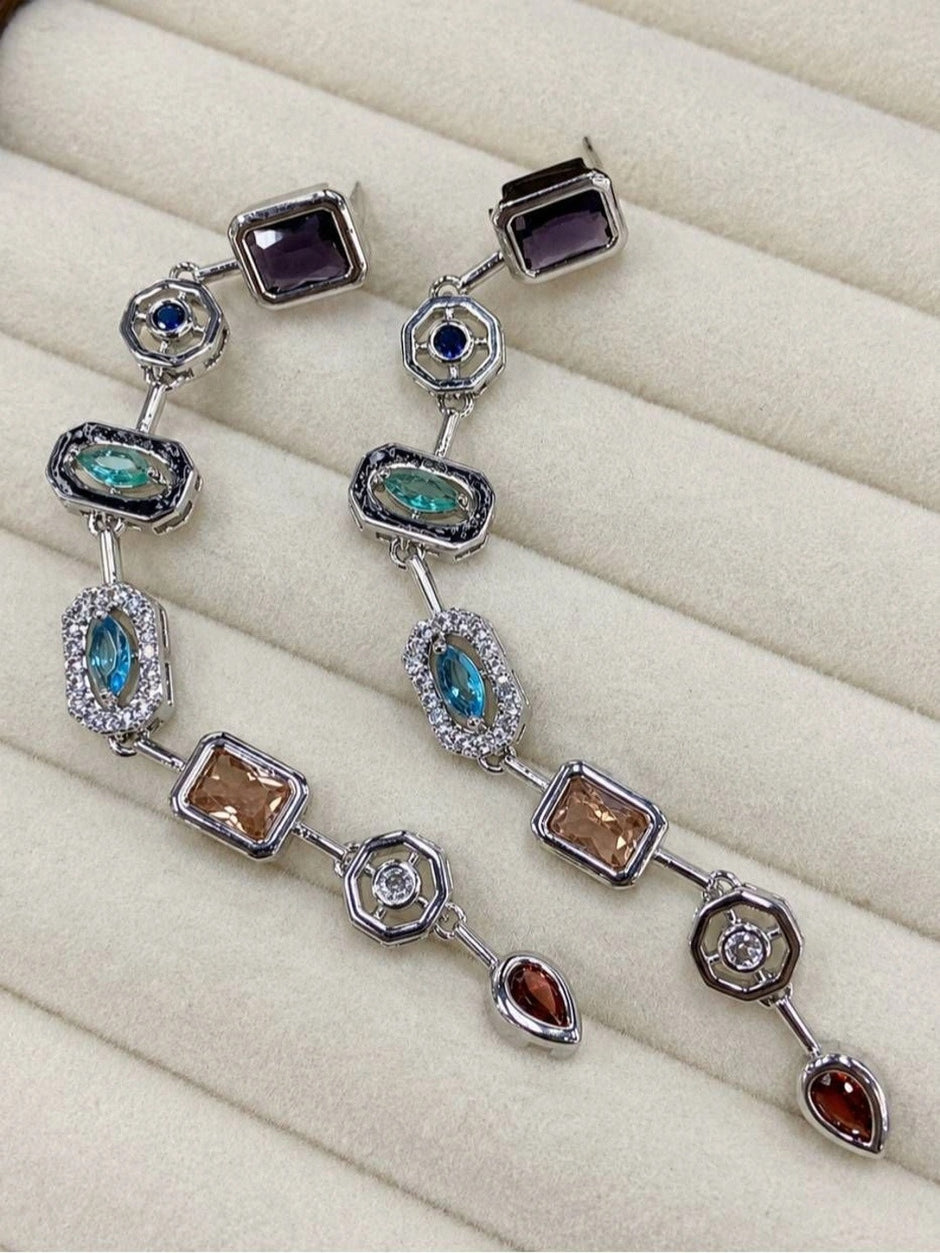 Flat overhead shot of the earring pair in a cream jewellery tray showing the full articulated chain link drop and all geometric stone stations