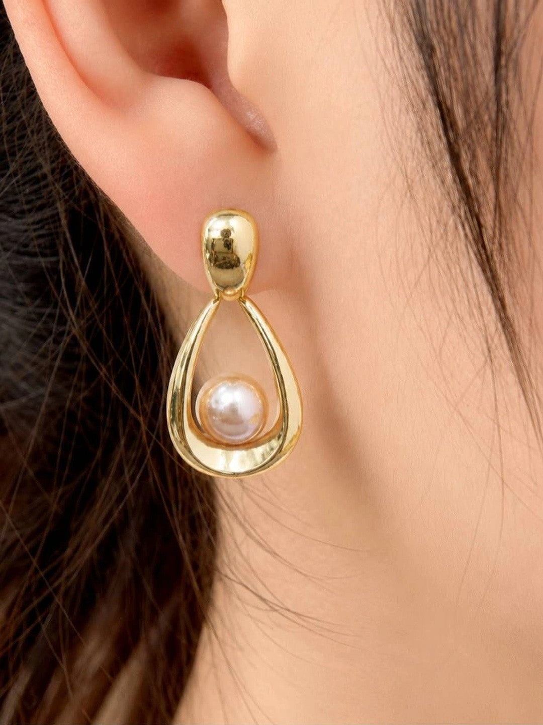 Single gold-plated pearl teardrop earring worn on a model's ear showing drape and scale
