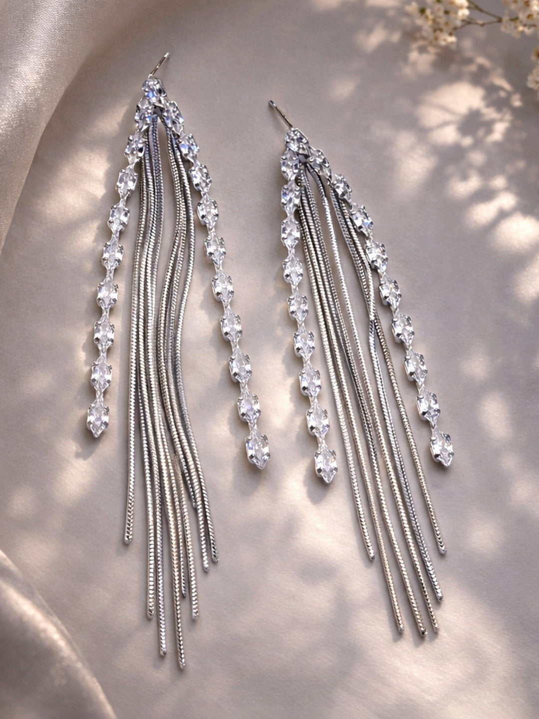 Pair of silver tassel drop earrings with marquise CZ stones laid flat on satin fabric