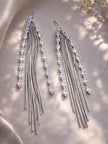 Pair of silver tassel drop earrings with marquise CZ stones laid flat on satin fabric