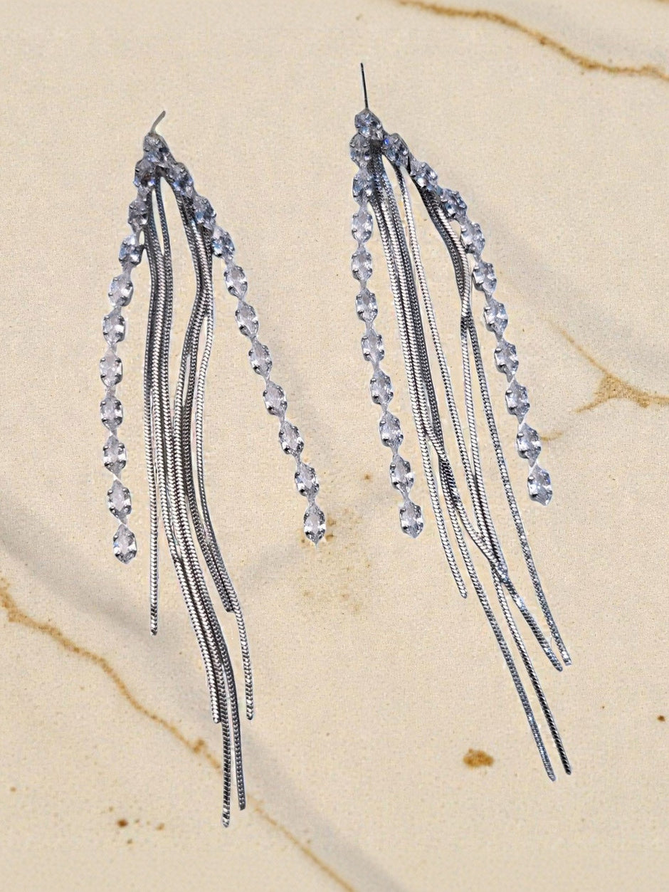 Two silver snake-chain tassel earrings with CZ stone line displayed on marble surface