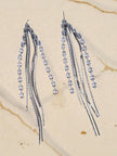 Two silver snake-chain tassel earrings with CZ stone line displayed on marble surface