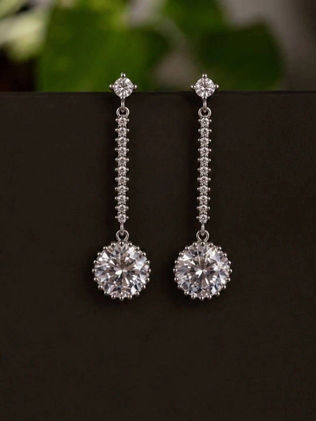 Pair of silver rhodium-plated cubic zirconia halo drop earrings against a dark background