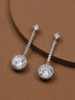 Silver-tone CZ halo drop earring pair laid on a warm brown display surface at an angle