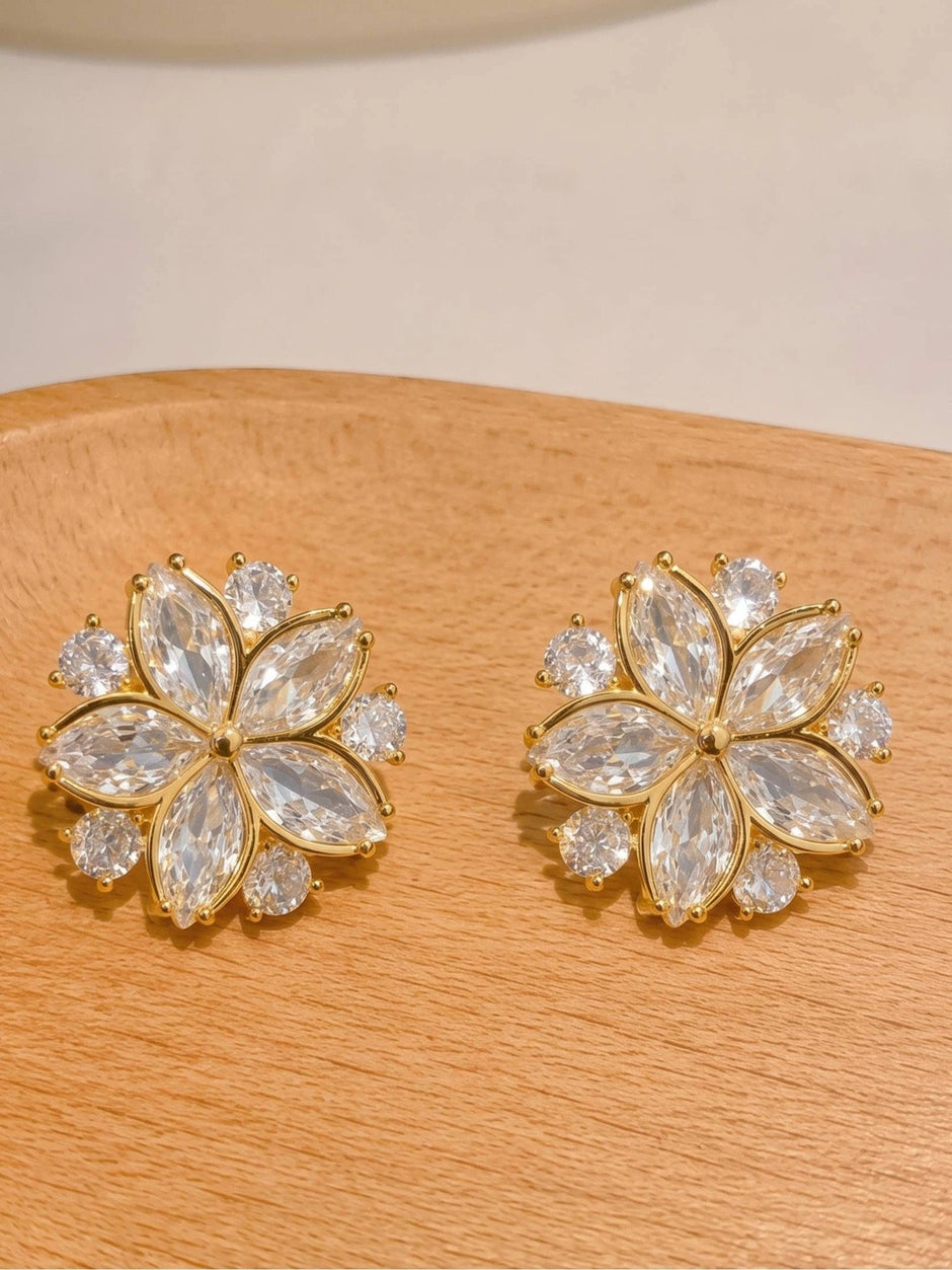 Pair of gold-plated flower stud earrings with marquise and round zirconia stones displayed on wooden surface