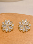 Pair of gold-plated flower stud earrings with marquise and round zirconia stones displayed on wooden surface