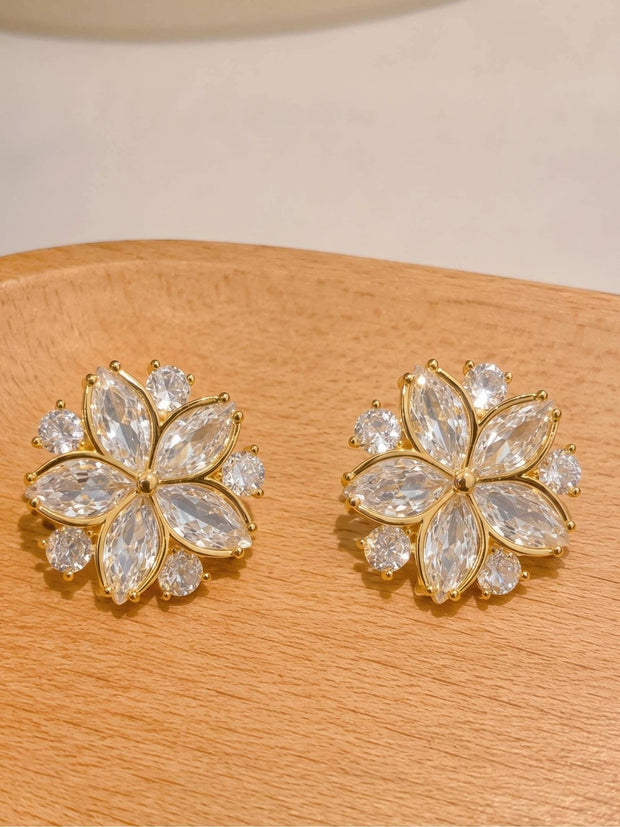 Pair of gold-plated flower stud earrings with marquise and round zirconia stones displayed on wooden surface