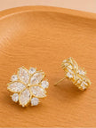 Front and side view of gold-plated zirconia floral stud earrings showing push-back post on wooden surface