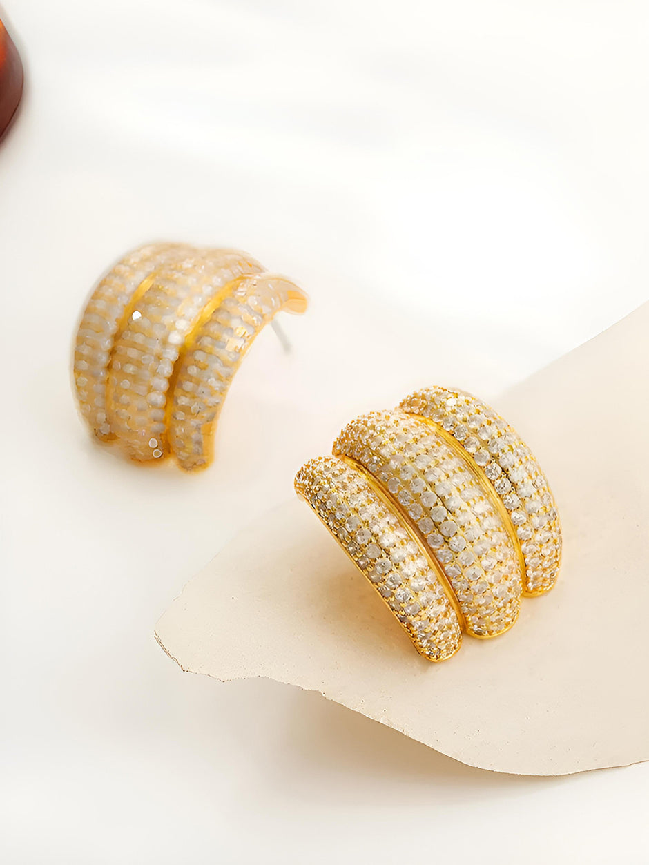 Pair of gold-plated chunky hoop earrings with pave cubic zirconia, displayed on a beige surface