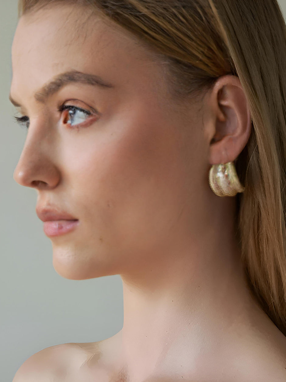 Side profile of blonde model wearing a gold chunky hoop earring with textured finish
