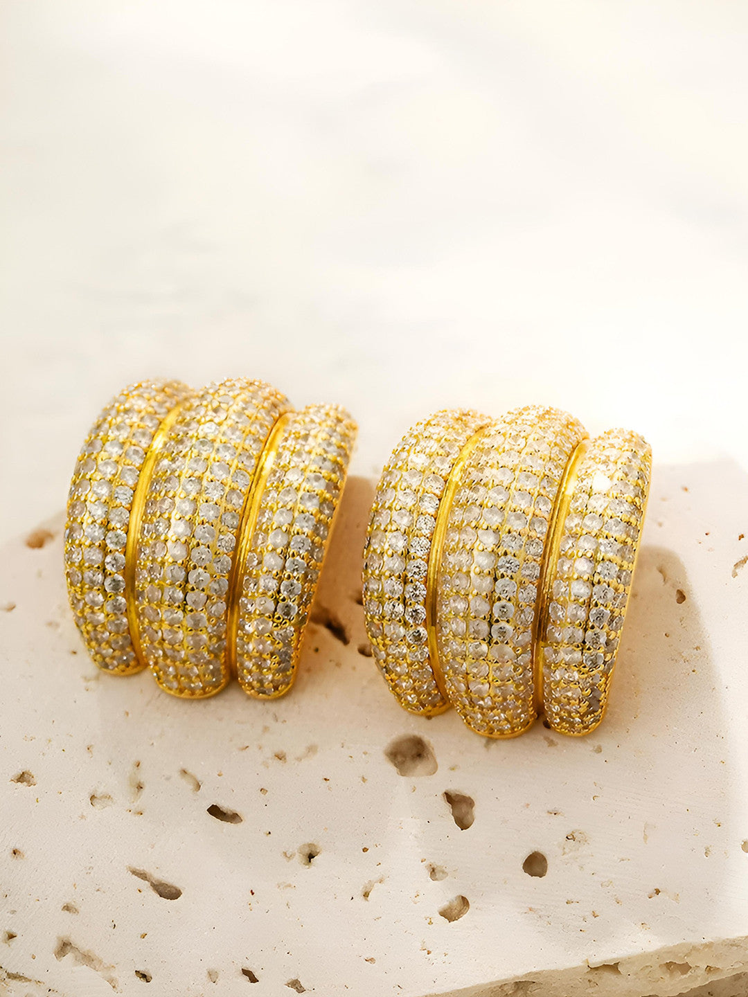 Both gold-plated CZ chunky hoop earrings placed side by side on a textured stone surface