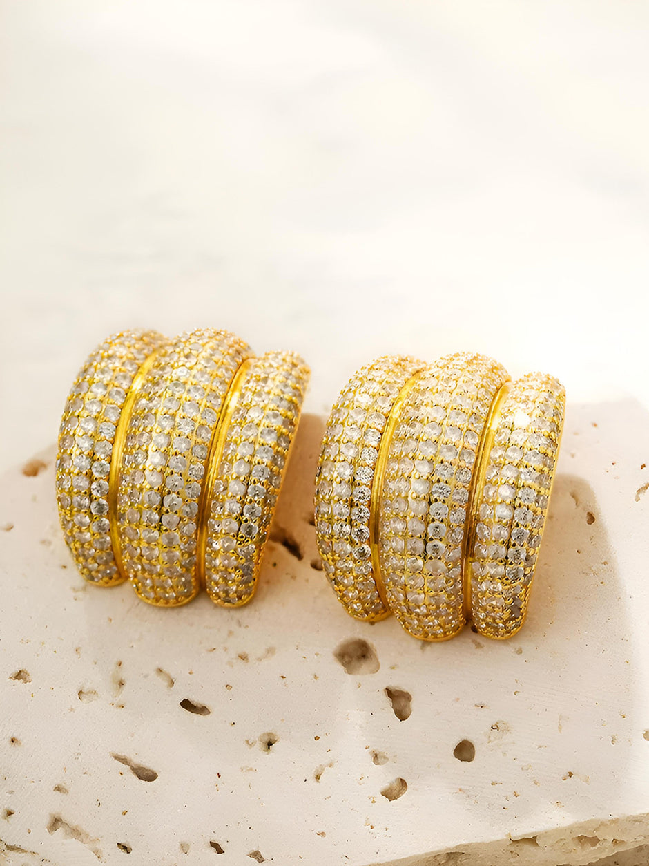 Both gold-plated CZ chunky hoop earrings placed side by side on a textured stone surface