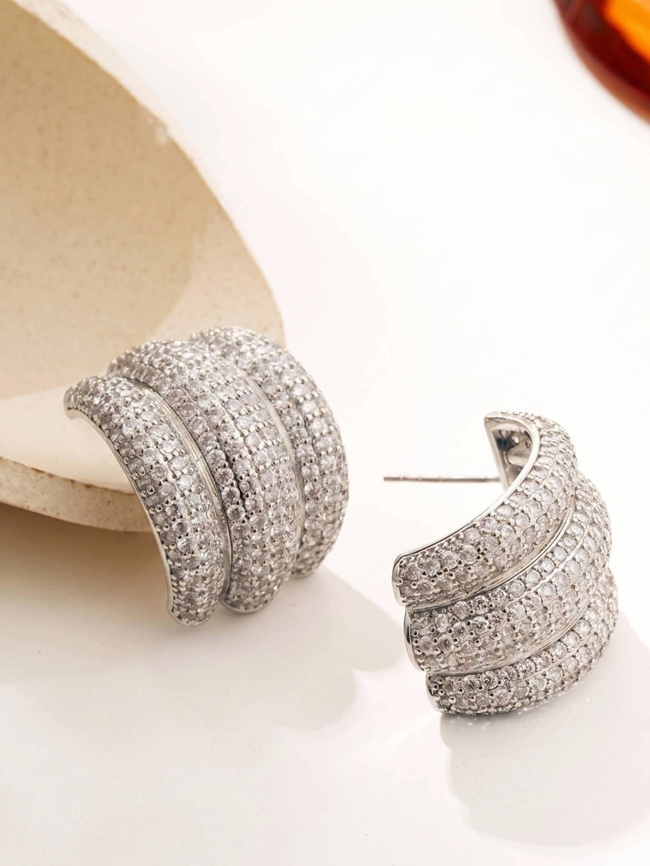 Pair of silver cubic zirconia triple half-hoop earrings displayed on a white surface with a cream prop