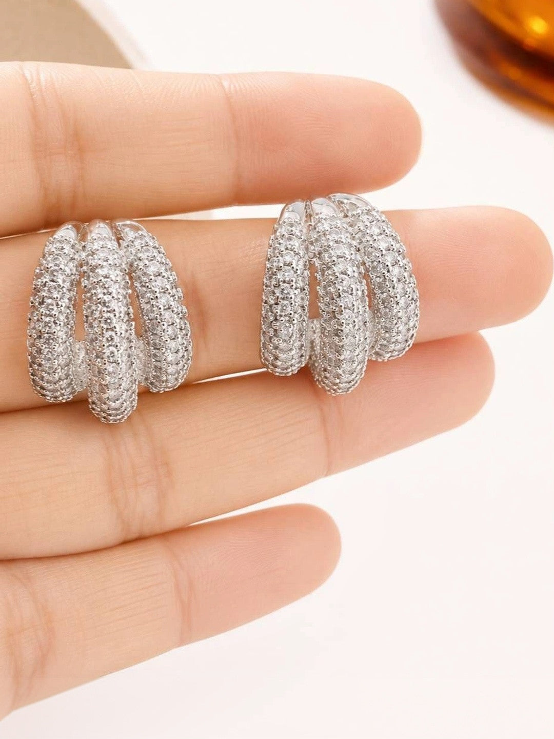 Both silver pavé triple hoop earrings held flat in an open palm to show scale and detail
