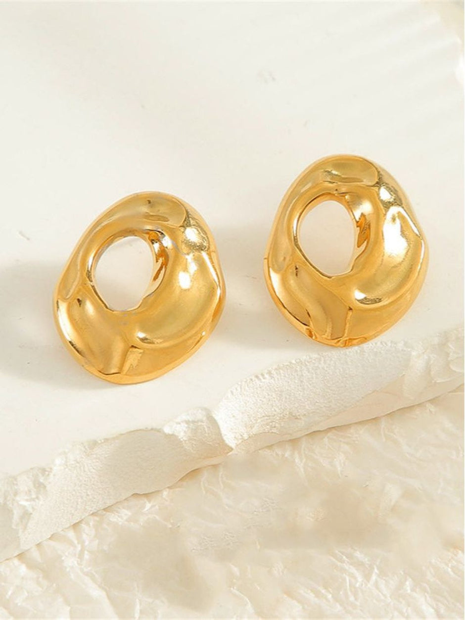 Pair of gold-plated chunky hollow oval stud earrings displayed flat on white surface with fabric