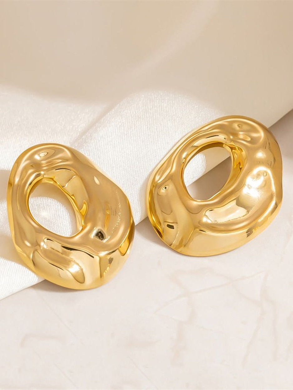 Two gold-plated hollow oval earrings leaning against white fabric showing sculptural molten texture