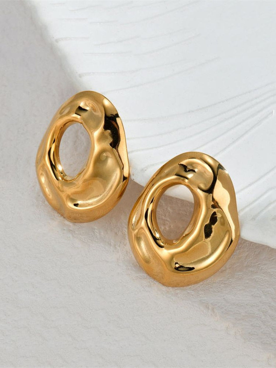 Gold-plated hollow oval stud earrings resting on white textured surface showing high-shine finish
