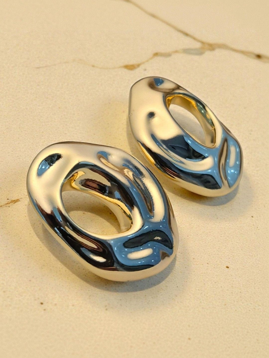 Silver-tone chunky hollow oval stud earrings placed on beige marble surface showing mirror polish