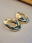 Close-up of silver-tone hollow oval earrings on cream background highlighting reflective curved surface