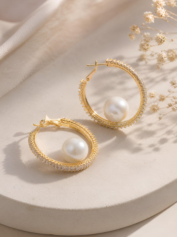 Pair of gold-plated CZ hoop earrings with faux pearl, styled on a cream surface with dried flowers