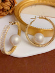 Two gold-plated pearl hoop earrings displayed against a gold frame and white ceramic surface