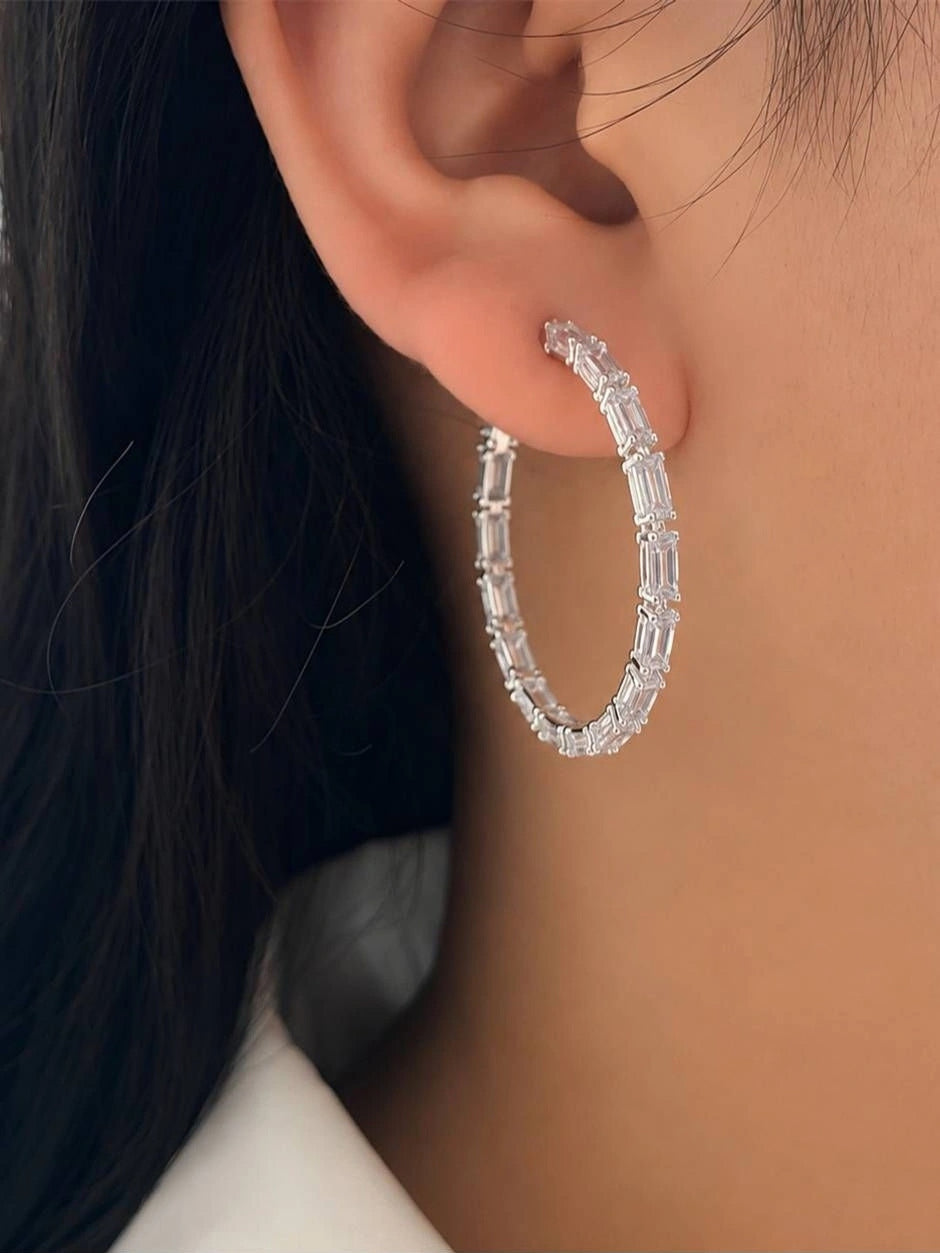 Silver cubic zirconia hoop earring worn on a woman's ear, showing full circular silhouette and baguette stone detail
