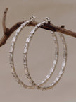 Pair of silver CZ hoop earrings resting on a wooden branch, showing baguette and round stone alternating pattern