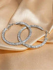 Two silver cubic zirconia hoop earrings overlapping on champagne satin, full circular form and all-around stone setting visible
