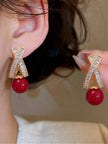Gold-plated crystal X-drop earring worn on ear beside matching earring held in hand