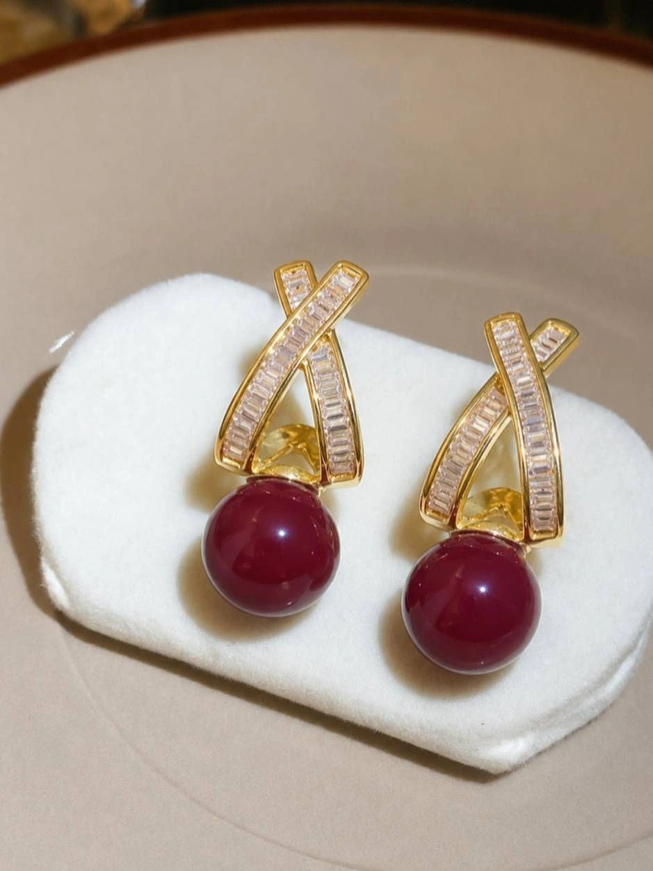 Two gold-plated red bead drop earrings displayed flat on white velvet jewellery pad