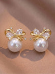 Pair of gold-plated bow stud earrings with faux pearl and cubic zirconia stones on a pink fabric surface