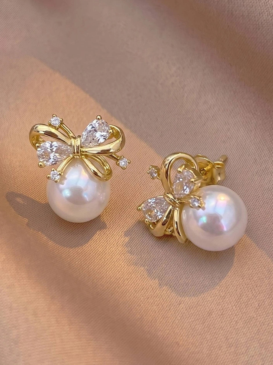Close-up of gold bow pearl stud earrings showing front and side angles on pink fabric