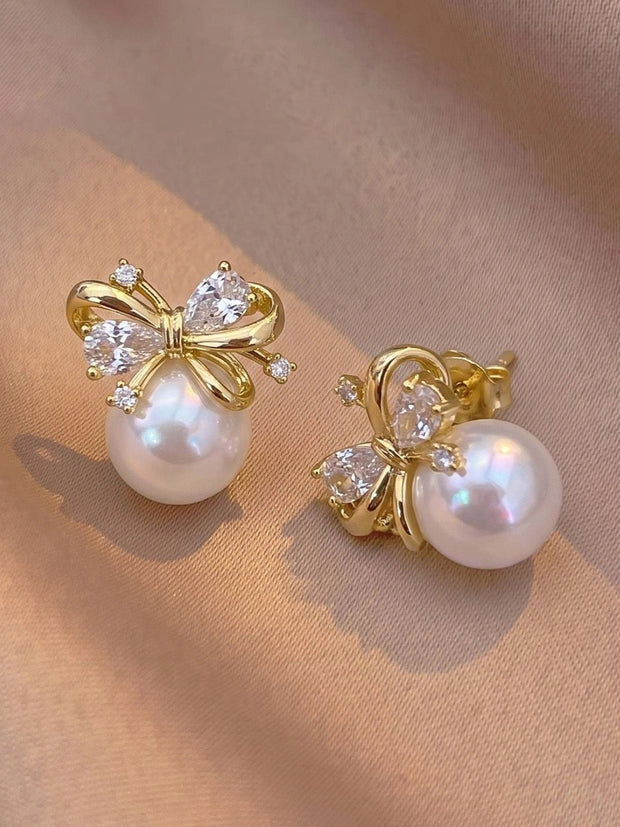 Close-up of gold bow pearl stud earrings showing front and side angles on pink fabric