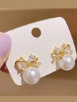 Both gold-plated pearl bow earrings pinned on a white jewellery display card held by hand