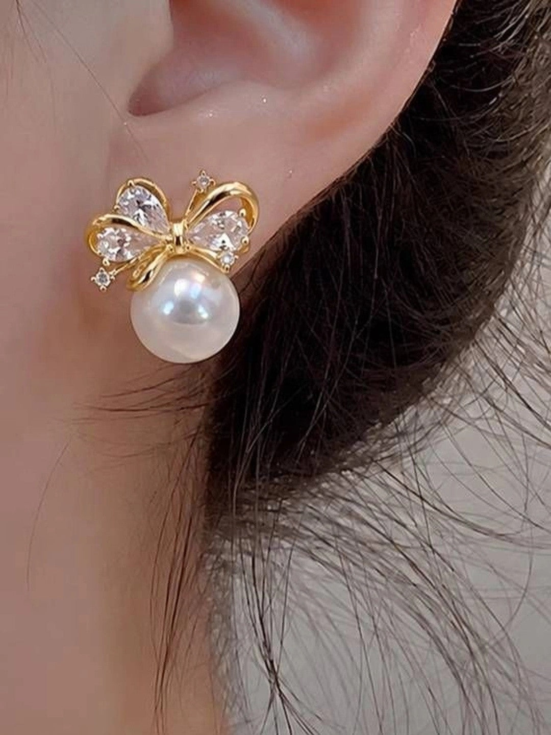 Single gold pearl bow stud earring worn on a model's ear showing real-size scale