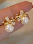 Two gold-plated pearl bow stud earrings resting on a model's fingertips showing CZ detail