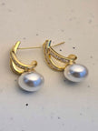 Pair of gold-plated pearl drop earrings with baguette crystals on a white marble surface, angled side view