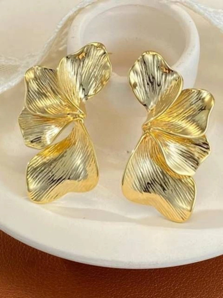Pair of gold-toned ribbed floral petal drop earrings resting on a white ceramic dish