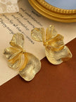 Gold-toned petal drop earring pair displayed on aged paper beside a gold-framed mirror