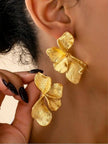 Model wearing gold-toned floral petal drop earring on ear while holding the second earring