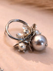 Close-up of a single silver hoop earring with grey pearl cluster and petal charms on a beige surface