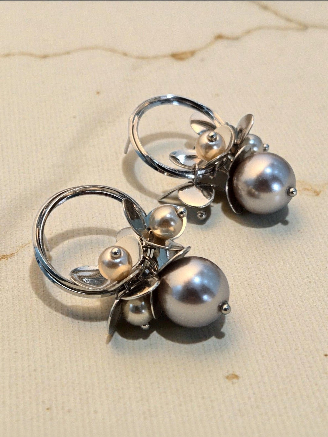 Pair of silver pearl cluster hoop earrings lying side by side on a cream textured background