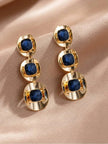 Pair of gold-plated blue crystal triple-drop earrings laid flat on rose satin fabric, front view